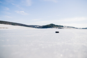 Hockey puck on a frozen lake in winter against the background of mountains.