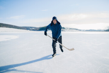 Fototapeta na wymiar Senior man with hockey stick skating on ice in winter. Looking into the camera.