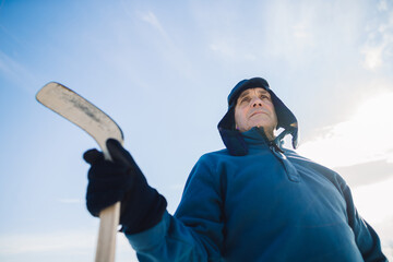 Portrait of an elderly man with a hockey stick against the background of the sky.