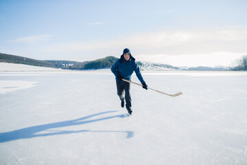 Senior man on ice skates with hockey stick on frozen lake in winter. Hobby concept of elderly...