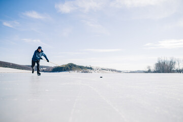 Fototapeta na wymiar An elderly man practices stricking the puck with hockey stick on a frozen lake in winter.