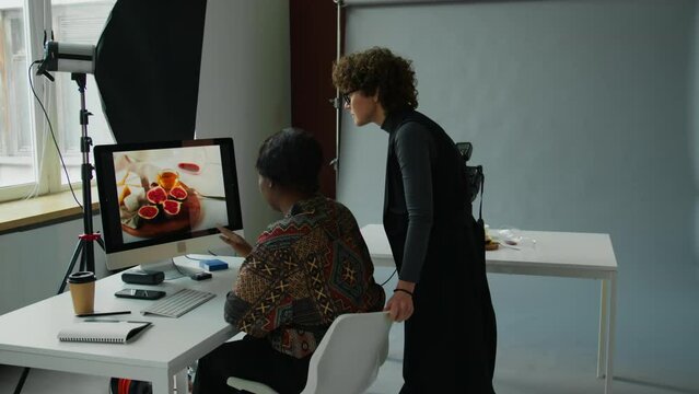 Female photographer showing reference image on computer screen to food stylist getting ready for shoot day in studio