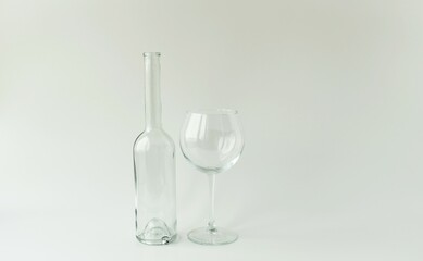 On a light background there is an empty glass bottle and an empty glass on a long stem.  Concept glassware, zero waste, excessive alcohol consumption.  Foreground, background, front view.