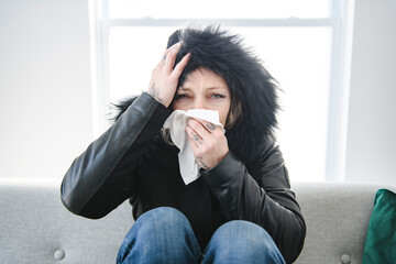 woman sit at home in jackets. The house is very cold. sits on sofa without heating.