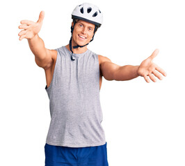 Young handsome man wearing bike helmet looking at the camera smiling with open arms for hug. cheerful expression embracing happiness.