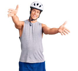 Young handsome man wearing bike helmet looking at the camera smiling with open arms for hug. cheerful expression embracing happiness.
