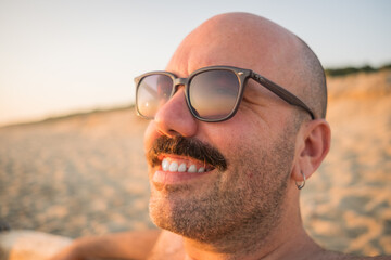 close up portrait of caucasian male wearing sunglasses with moustache sit on the beach summer holiday happy 