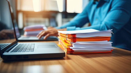 Close-up of a man's hands typing on a laptop keyboard, with a stack of paperwork beside them - obrazy, fototapety, plakaty