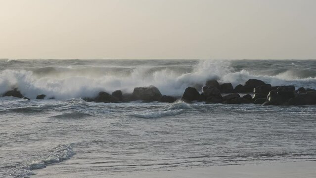 Large waves in the Mediterranean Sea crash against the rocks, depicting a scene of stormy weather at sea.