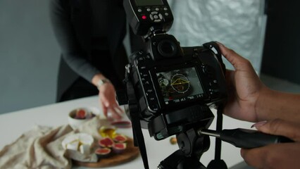Close up view of hands of professional female photographer setting digital camera as stylist arranging food on table before studio photoshoot