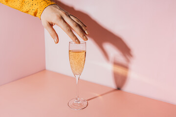 Lady's hand over a glass of champagne against a pink background.