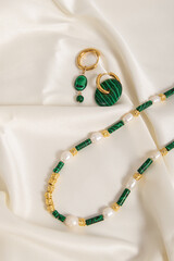 Set of jewelry made of malachite and pearls. Necklace and earrings on silk background