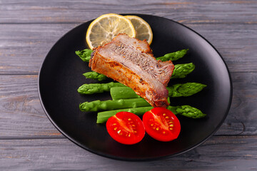 Grilled ribs with green asparagus, tomatoes and lemon on a plate