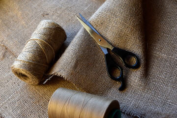 Yellow skeins of thread and scissors on a background of burlap. Yellow coarse cloth threads and...