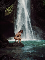 Woman in bikini enjoying near waterfall. Traveler young girl posing on waterfall
