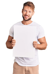 Young caucasian man holding blank empty banner looking positive and happy standing and smiling with...