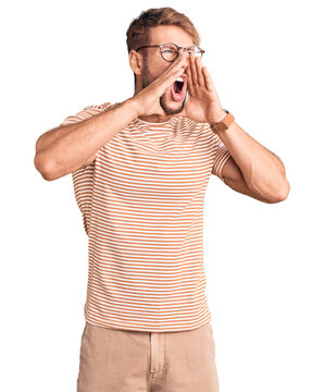 Young caucasian man wearing casual clothes and glasses shouting angry out loud with hands over mouth