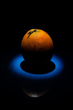 Fotograf&iacute;a de una naranja de color naranja sobre una superficie azul, con reflejos y en clave baja. Colores complementarios.