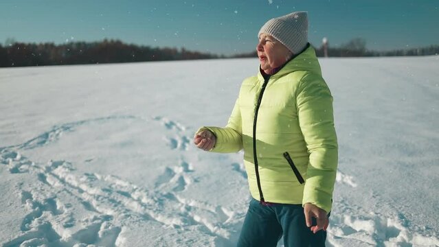 Happy beautiful 50s woman blowing snowflakes from her hands to her dog irish setter enjoying winter snow outdoors activity in winter day holiday. People and animals together having fun and smiling