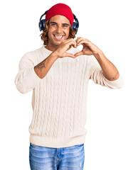 Young hispanic man listening to music using headphones smiling in love doing heart symbol shape with hands. romantic concept.