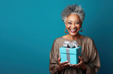 Beautiful African American mature woman 50, 60, 70 years old on a blue background holding a large gift box, holiday surprise, compliment bonus for birthday anniversary