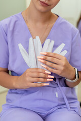 Portrait of a manicurist young girl holding nail file for processing nails, wearing purple uniform. Manicure and pedicure master in a beauty salon, training, work break, teenager employee, nail care