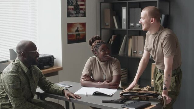 Full medium shot of smiling diverse male and female cadets in camouflage uniforms talking before training class in military academy