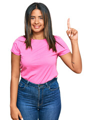 Young latin girl wearing casual clothes showing and pointing up with finger number one while smiling confident and happy.