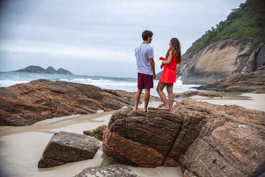 Young couple, hugging, talking, standing on a rock at the beach.