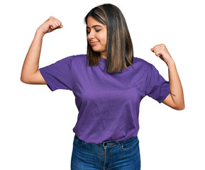 Young hispanic girl wearing casual purple t shirt showing arms muscles smiling proud. fitness concept.