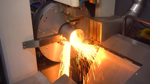 Slow motion, close up: automatic cnc laser cutting machine working with cylindrical metal workpiece with many sparks. Metalworking, industrial, manufacturing, technology and equipment concept