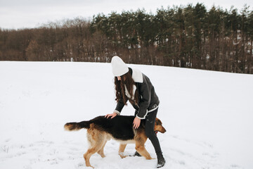 Young woman walk the dog German Shepherd in winter field forest, running playing with snow, training the animal in harsh conditions, wind blowing. Christmas Time, New Year

