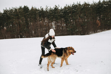 Young woman walk the dog German Shepherd in winter field forest, running playing with snow, training the animal in harsh conditions, wind blowing. Christmas Time, New Year
