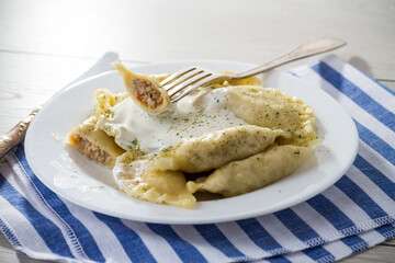 cooked dumplings with meat, spices and sour cream, in a plate on a light wooden table.