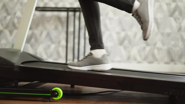 Lady sprints on treadmill indoors closeup. Fit lady with slender legs works out on motorized exerciser in home fitness area. Physical session