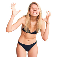 Young beautiful blonde woman wearing bikini shouting frustrated with rage, hands trying to strangle, yelling mad