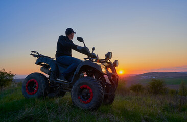 a man on a quad bike looks at the sunset,a young man enjoys the sunset on the mountain