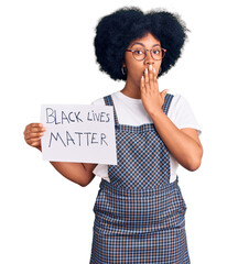 Young african american girl holding black lives matter banner covering mouth with hand, shocked and...