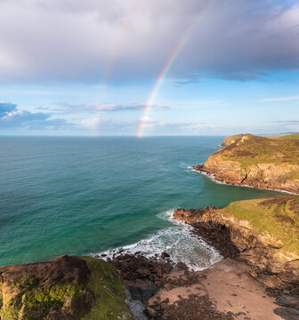 Aerial view of swimmer at secret cove with a rainbow in the sea, Talland Bay, Cornwall, United Kingdom.