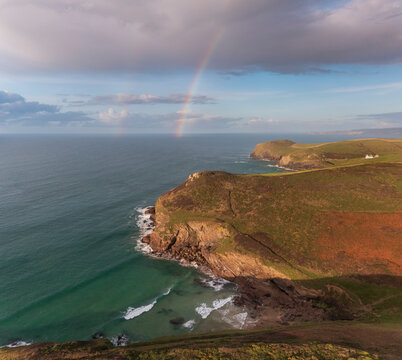 Aerial view of swimmer at secret cove with a rainbow in the sea, Talland Bay, Cornwall, United Kingdom.