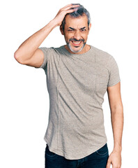 Obraz premium Middle age hispanic with grey hair wearing casual grey t shirt confuse and wonder about question. uncertain with doubt, thinking with hand on head. pensive concept.