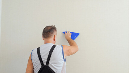 Senior Caucasian man with dark hair makes repairs, glue the wallpaper, new design, home renovation.