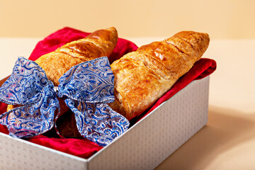 Fresh delicious croissants lie in gift box on red velour fabric. Beautiful blue bow adorns the...