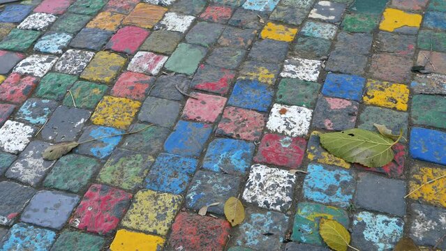 Cobblestone pavement stones painted in various colors. Autumn leaves fallen on an artistic colorful cobble stone road, panning shot.