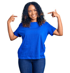 Young african american woman wearing casual clothes looking confident with smile on face, pointing...