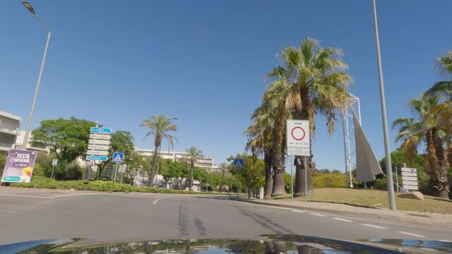 First person view, FPV, from dashcam of car driving along the Algarve Coast in Portugal in Albufeira, driving in the city. Road trip video in POV, with blue sky