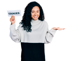 Young hispanic woman with curly hair holding cookies banner celebrating achievement with happy smile and winner expression with raised hand