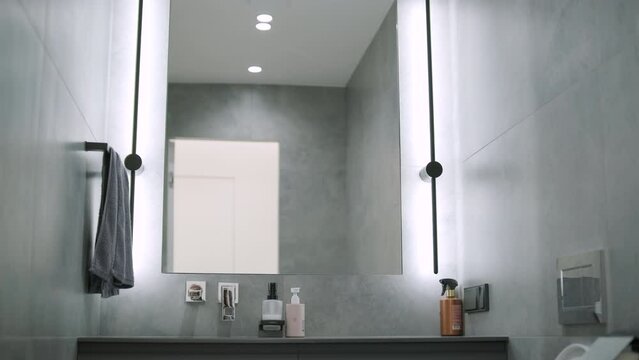 Modern minimalistic bathroom interior design with grey stone tiles, black furniture, eucalyptus in glass vase, round mirror. Aesthetic simple interior design concept.
