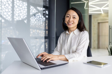 Portrait of online support worker, asian woman with headset phone smiling and looking at camera,...