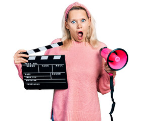 Young caucasian woman holding video film clapboard and megaphone afraid and shocked with surprise...